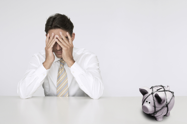Man with a piggy bank next to him, and with his head in his hands